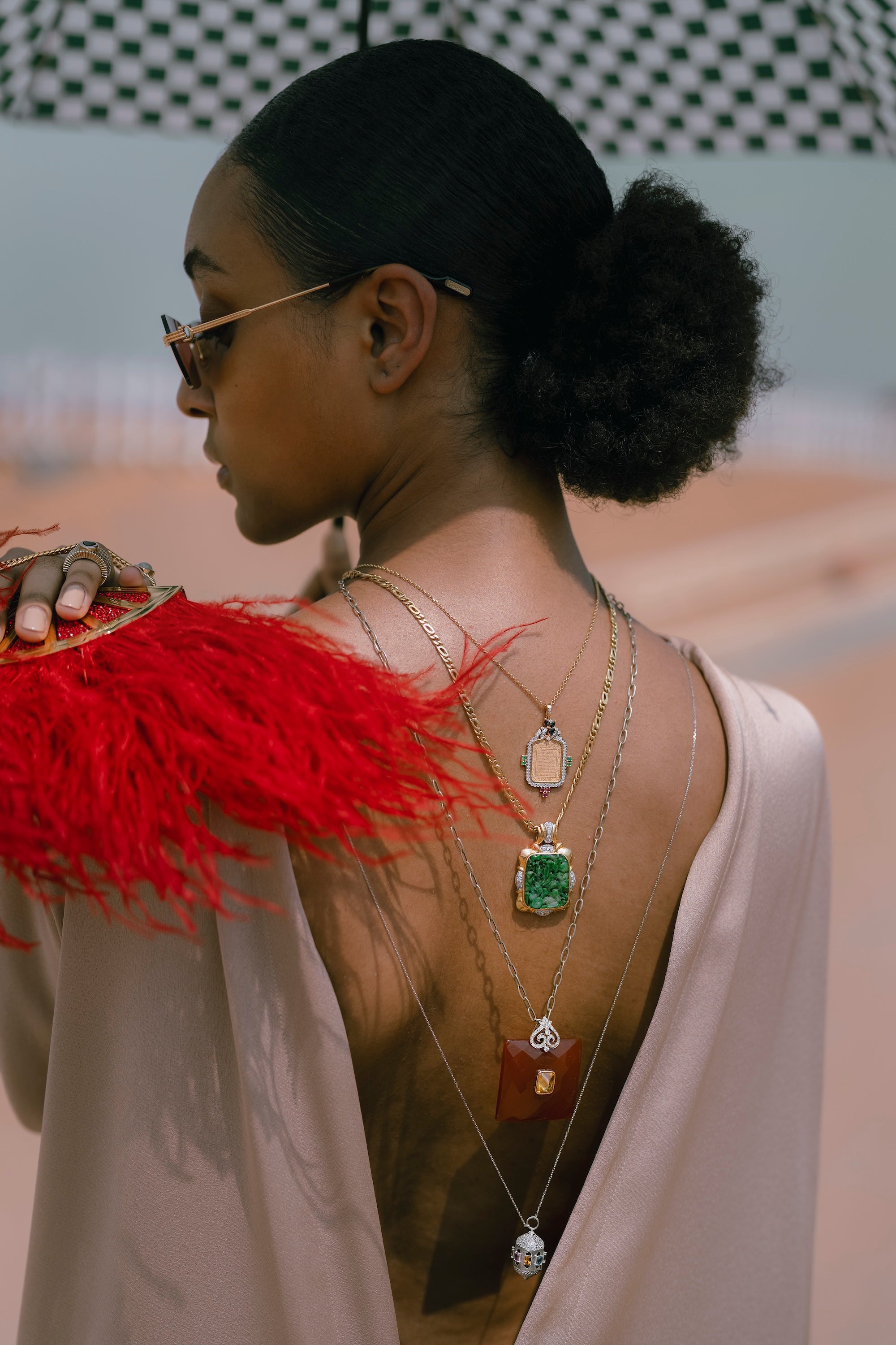 Woman wearing sunglasses and a red feathered shoulder piece with visible jewelry.